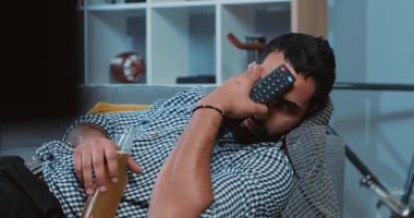 Bira içen genç ve çekici bir adam TV izlerken kumandayı tutarak evde yalnız başına uzanır şişeci çocuk kanepe mutlu alkol yaşam tarzı portresi TV 'de yavaş çekimde oturur.