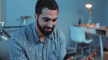 Çevrimiçi satın alan mutlu genç bir adam kanepe üzerinde bir telefon ve bir kredi kartı kullanıyor ev telefonu müşterisi kapalı yaşam tarzı akıllı iş dünyası internet teknolojisi bankacılığı nakit tutuyor