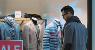 Çekici bir adamın Noel hediyeleriyle bir alışveriş merkezinde gülümseyerek Noel Baba dekorasyonlarına bakarken yavaş çekim aşk portresi tasarlarken.