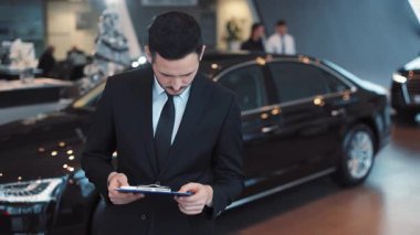 Sakallı ve belgeyi dikkatlice inceleyen çekici bir genç. Yeni arabaların arka planlarını silkeleyen takım elbiseli adam şaşırdı..