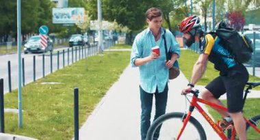 NEW YORK - 5 Nisan 2017: genç yakışıklı beyaz adam sokakta yürüyor ve kahve içiyor. Bisikletçi adamın yanına gidip bir fincan kahveye dokunuyor. Adam kızıyor. Bahar mevsimi.