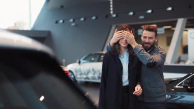 Genç adam doğum günü için karısına araba veriyor. Araba galerisindeki çekici çift. Mutlu genç kadın yakışıklı adama sarılıyor..