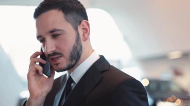 Genç işadamı cep telefonundan konuşuyor. Sakallı çekici bir adam önemli bir konuşma yapıyor. Koyu takım elbiseli ve kravatlı adam.