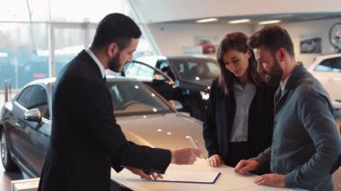 Yeni araba alan mutlu genç çift. Makine satıcısı ve alıcı el sıkışıyor, kontrata imza atıyor. Başarılı bir anlaşma yapan makine satıcısı.