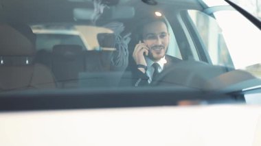Siyah saçlı, takım elbiseli, kravatlı, yeni arabasında oturan çekici bir genç. Başarılı, kendinden emin iş adamı akıllı telefonla konuşuyor, gülüyor..