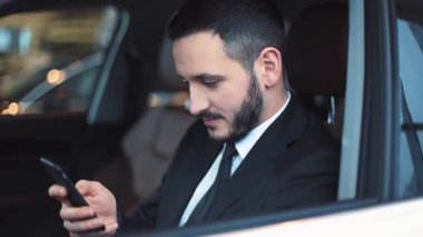 Arabada oturan sakallı yakışıklı adam. Genç adam akıllı telefon ekranına bakıyor, mesajları okuyor ve gülüyor. Yakın plan..