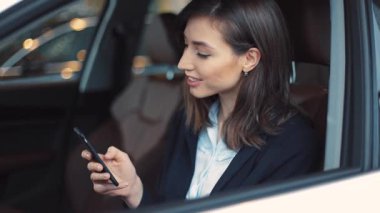 Koyu renk kısa saçlı güzel bir kadın araba salonunda oturuyor. Akıllı telefon ekranına bakan, erkek arkadaşından mesaj okuyan bir kız. Gülümsüyor. Sohbet..