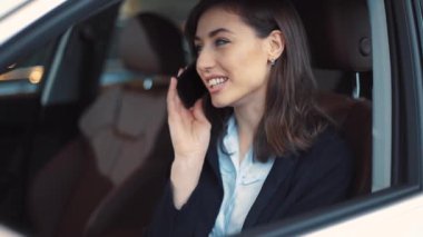 Genç, gülümseyen, kahverengi saçlı, mavi gözlü, cep telefonuyla konuşan bir kadın. Yeni beyaz arabanın salonunda oturan kız..