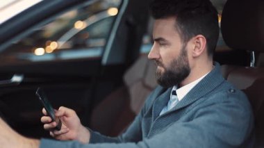 Direksiyonda oturan sakallı ve akıllı telefon ekranına bakan ciddi bir genç adam. Elinde siyah akıllı telefon tutan ve mesaj okuyan bir adam..