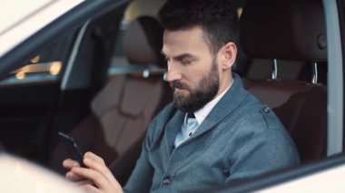Mavi kazaklı bir iş adamı yeni arabanın direksiyonunda oturuyor. Sakallı konsantre genç adam akıllı telefondan mesaj yazıyor..