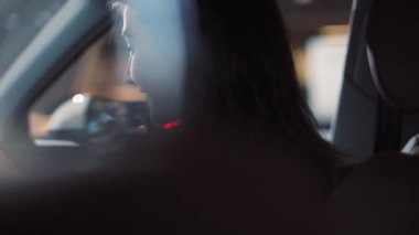 Genç ve güzel bir kadın arabada oturuyor ve dikkatle sürücüye bakıyor. Mavi gözlü güzel kız gülümsüyor.