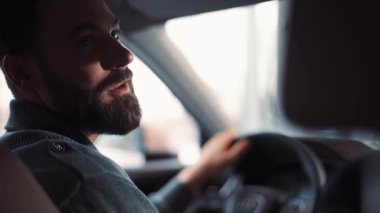 Araba direksiyonunda oturan sakallı yakışıklı genç adam konuşuyor. Adam araba seçiyor, sandalyeye, tekere dokunuyor, otomobilin içini görüyor. .