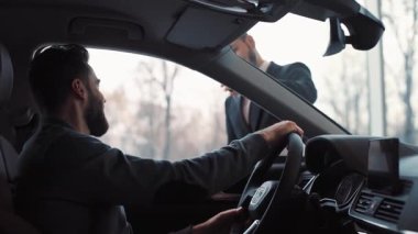 Arabaların içinde oturan çekici genç bir adam. Araba satıcısının danışmanı alıcıya anahtarları veriyor. Adam dikiz aynasını ayarlıyor, dikkatlice etrafına bakıyor. Yakın plan..