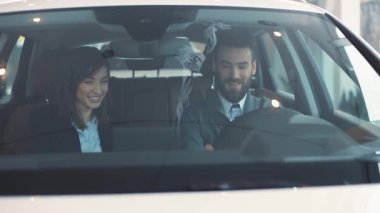 Aşık mutlu çift arabada oturuyor. Kısa saçlı, güzel esmer, gülümseyen, erkeklere sorular soran. Arabanın içini inceleyen gençler.