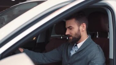 Günlük kıyafetli bir adam arabanın kapısını açıyor ve sürücü koltuğuna oturuyor. Satıcı anahtarları veriyor. Sakallı, sakallı, kendine güveni tam genç bir adam. Arabanın içini aydınlatıyor..