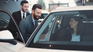 Genç bir çift araba galerisinde araba seçiyor. Çekici bir kız. Çekici bir gülümsemesi var. Arabanın içinde oturuyor..