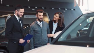 Araba seçen genç bir çift. Danışman modelden bahsediyor, kuaföre gitmeyi teklif ediyor. Büyük şehirde popüler araba galerisi..