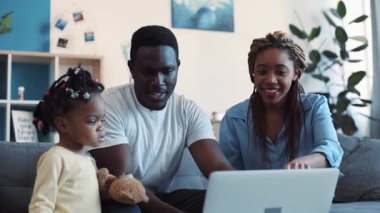 Dizüstü bilgisayar kullanan ve oyuncak bebeklerini gösteren sevimli genç bir çift. Anne komik hareketler yapıyor. Aile zamanı, eğlenmek. Yavaş çekim, kamera dengeleyici çekim