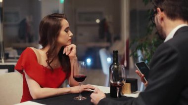 İnanılmaz derecede kadınsı Ukraynalı, kahverengi saçlı ve bukleli bir kız, tarihte sıkıcı, başka yöne bakıyor. Kafkasyalı bir adam akıllı telefondan saate bakıyor. İçeride. İyi akşamlar..