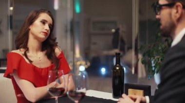 Uzun saçlı, erkek arkadaşına bakan, kolları bağlı, şüpheli, çekici bir Ukraynalı kız. Klasik kıyafetler giymiş genç bir çift masada şarapla konuşuyor..
