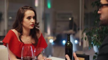 Uzun saçlı, erkek arkadaşına bakan, kolları bağlı, şüpheli, çekici bir Ukraynalı kız. Klasik kıyafetler giymiş genç bir çift masada şarapla konuşuyor..