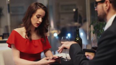 Kırmızı elbiseli çekici kız ve restoranda masada oturan gözlüklü genç adam akıllı telefonlardan yeni fotoğraflar izliyorlar. Kur yapma