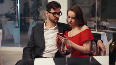 Güzel Ukraynalı kız arkasına yaslanmış, akıllı telefona bakıyor, restoranda interneti araştırıyor. Erkek ve kadın buluşuyor. İyi akşamlar..