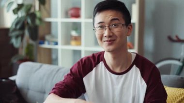 İnanılmaz bir portre mutlu çekici başarılı gözlüklü genç Çinli adam kameraya bakıyor kanepeye oturuyor gülümsüyor Asyalı yakışıklı iş adamı yakışıklı yakışıklı adam yavaş çekimde yaklaş