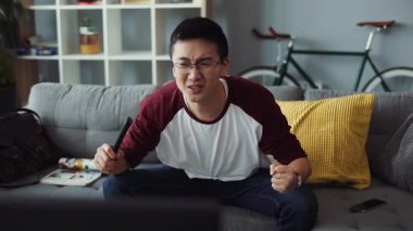 Üzgün, çekici, gözlüklü genç Çinli adam kanepede oturur ve TV 'yi açar. Ev bakımı teknolojisi erkek işi. Boş zamanlardan sıkılan video kanepe portresi.