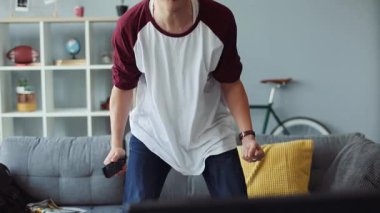 Gözlüklü yakışıklı Çinli adam evde uzaktan kumandayı tutuyor televizyon evi teknolojisi erkek iş dünyası mutlu video kanepe portresi yavaş çekimde gülümsüyor.