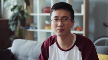 Kapalı yüz hayal kırıklığına uğramış, gözlüklü, çekici genç Çinli adam evdeki kanepede oturup kamera evine bakıyor. Erkek işi, boş zamanların üzücü videosu. Kanepe portresi yavaş çekimde.