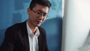 Gözlüklü genç Çinli bir portre ofis işindeki ekrana bakmak için bilgisayar kullanıyor. İnternetle yüz yüze iş adamı. Dizüstü bilgisayar işadamı.