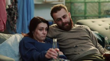 Üzgün alkolik adam ve kadın kanepede oturur evde içki içerler içki içerler, erkek göbeği bağımlılığı yetişkin alkolizmi tek başına sorun portre istismarı depresyonu ağır çekimde strese sebep olur.