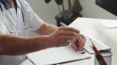 Steteskoplu bir doktor masada oturuyor, belgeleri yazıyor. Hasta bir hasta X-ray 'i elinde tutuyor ve terapiste veriyor. Sağlık çalışanı röntgene bakıyor. Konuşma.