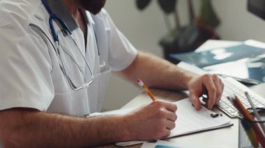 Boynunda steteskop olan beyaz bir doktor doktorun ofisinde oturmuş, hastanın elini sıkıyor. İçeride. Şehrin popüler kliniği..