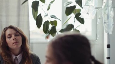 Gri hırkalı, yorgun bir anne kızıyla konuşuyor. Yatakta yatan tatlı hasta kız. Hastanede kuluçka dönemi. Yakın plan..