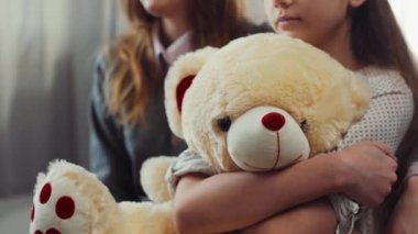 Uzun kahverengi saçlı, kızının yanında oturan genç, çekici, mutsuz bir kadın. Küçük hasta kız, doldurulmuş güzel bir oyuncağa sarılıyor. Klinikte iki kadın.