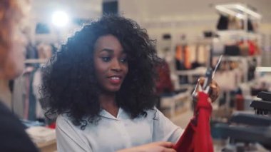 Kıvırcık saçlı arkadaşlar alışveriş merkezinde birlikte kıyafet seçiyorlar. Afro-Amerikan kadın gülümsüyor. Moda kızı fitness teknolojisi.