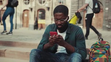 Gözlüklü üzgün Afrikalı Amerikalı genç adamı kapatın. Şehirde telefon kullanıyor. Ciddi teknoloji işadamları meşgul.