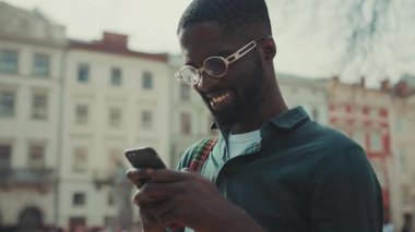 Gözlüklü Afrikalı Amerikalı telefon kullanıyor. Günbatımı teknolojisinde yürüyor. İş adamları meşgul.