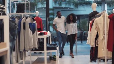 Giysi mağazasından kıyafet seçen Afrikalı genç bir çift. Gülümseyen bir aile kadını. Moda alışverişi yapan adam.