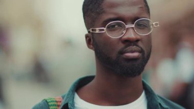 Gözlüklü genç Afrikalı Amerikalıyla yüzleş. Kameraya bak. Şehirde ciddi dur. Neşeli moda portresi.