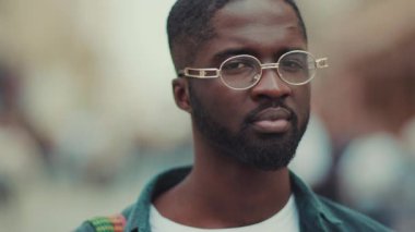 Çekici, gözlüklü genç Afrikalı Amerikalı kameraya bak. Gülümse. Yüzünde mutlu bir ifade var.