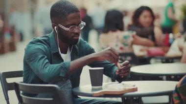 Çekici genç Afrikalı Amerikalı turist müzik dinliyor. Kulaklıkla sokakta kahve içiyor. Moda yüzlü, siyah kulaklık takıyor.