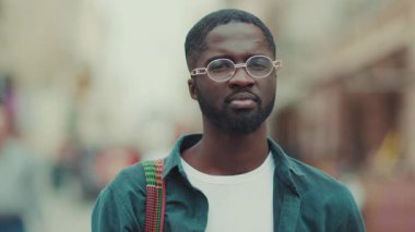 Kapalı yüzlü, gözlüklü genç Afrikalı Amerikalı kameraya bak. Gülümse. Şehrin dışında mutlu ol.