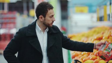 Yakından bakınca yakışıklı adam taze meyve portakalını süpermarketten seçiyor gülümsüyor yiyecek alışverişi yapıyor tezgahtarlık yapıyor yetişkin bakkal erkek organik ürün bulanık alışveriş merkezi satışı