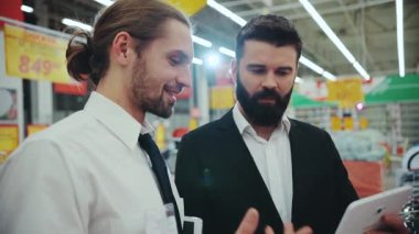 NEW YORK - 5 Nisan 2017: Genç sakallı adamla satış danışmanı konuşması. Teknoloji mağazasında dokunma tableti tableti kullan. Elektronik alışveriş teknolojisi. İnternet alışveriş merkezi yavaş çekim portresi.