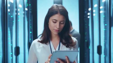 Odaklanmış bir kadın modern bir veri merkezinde son teknoloji gelişmelerini gösteren bir tablet kullanıyor.