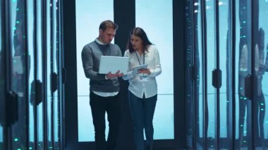 İki yetenekli profesyonel, çok sayıda sunucuyla dolu modern ve gösterişli bir veri merkezinde dizüstü bilgisayarlarıyla birlikte çalışıyor.