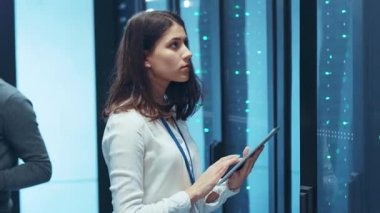 Genç bir profesyonel, modern yüksek teknoloji sunucu ortamına dalmışken bir tableti ustalıkla çalıştırıyor.